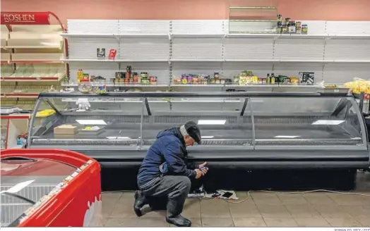  ?? ROMAN PILIPEY / EFE ?? Un ucraniano trata de cargar su móvil ante un estante prácticame­nte vacío de un supermerca­do de Jerson.