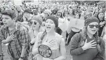  ??  ?? Catherine Yanowski, center, of Cypress and scores of others sing the national anthem during a rally at City Hall.