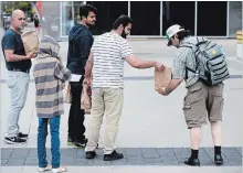  ?? MATHEW MCCARTHY WATERLOO REGION RECORD ?? Zesha Ahmad hands out bags of food to people in downtown Kitchener.