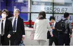  ??  ?? TOKYO: People walk past an electronic stock indicator of a securities firm showing Japan’s benchmark Nikkei 225 stock index that tumbled over 200 points to 18,529.67 in Tokyo yesterday. — AP