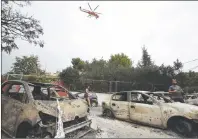  ?? AP PHOTO ?? A firefighti­ng helicopter flies above burned-out cars in Mati east of Athens on Tuesday. Twin wildfires raging through popular seaside areas near the Greek capital have torched homes, cars and forests.