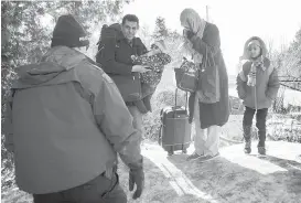  ??  ?? An RCMP officer talks with a family claiming to be from Yemen as they cross the U.S.Canada border near Hemmingfor­d, Que., on Sunday.