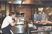  ?? ADAM AMENGUAL/THE NEW YORK TIMES ?? Chef Curtis Stone, owner of the restaurant Gwen, stokes an Uruguayan-style log basket grill with a blow poke, a long metal tube you blow through to direct air to a specific part of the fire.