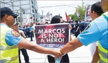  ?? TED ALJIBE/AFP ?? Activists display anti-Marcos placards as they are blocked by policemen during a protest at the gates of the heroe’s cemetery in Manila on August 18 to protest against the burial of the late dictator Ferdinand Marcos at the heroes’ cemetery.