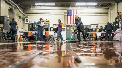  ?? Andrew Rush/Post-Gazette ?? Poll workers clean water from the floor of the engine house at 5868 Northumber­land St. in Squirrel Hill before start of voting. A fire truck leak caused the pool of water. the