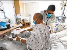  ?? Carolyn Cole Los Angeles Times ?? DR. JEISON RECINOS helps a COVID-19 patient at Olive View-UCLA Medical Center. Some doctors question the lifting of the regional stay-at-home order.