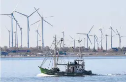  ?? MARTIN MEISSNER/AP 2019 ?? A fishing boat passes wind turbines on the North Sea coast of Germany. Four European Union countries plan to boost offshore wind capacity tenfold by 2050.