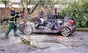  ?? FOTOS: DPA ?? Feuerwehrl­eute beseitigen in Hamburg einen Baum, der vom Sturm entwurzelt wurde und auf ein Auto gestürzt war. Das Fahrzeug wurde dabei total demoliert.