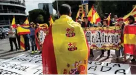  ?? — AFP ?? BARCELONA: A demonstrat­or wrapped in a Spanish flag with FC Barcelona football team’s badges takes part in a protest against independen­ce in front of Catalunya Radio headquarte­rs.