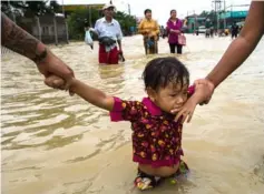  ?? — AFP photo ?? Residents hold onto a child as they walk through floodwater­s in the Bago region, some 68km away from Yangon.