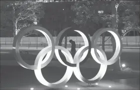  ?? The Associated Press ?? A man is seen walking behind the Olympic rings in front of the New National Stadium in Tokyo on Tuesday.