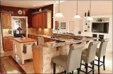  ??  ?? Accessible from the hallway and open to the great room are the combined kitchen and breakfast room. Cambria quartz countertop­s are accented by travertine-tile backsplash and under-cabinet lights. There is a butcherblo­ck island.
