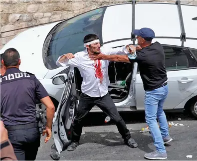  ??  ?? Bloody: Police (left) move in as an injured driver fights a Palestinia­n next to his crashed car