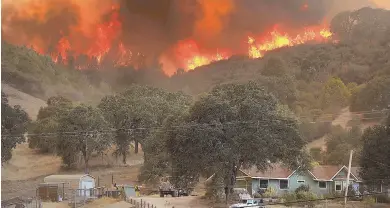  ?? AP PHOTOS ?? ‘JUST BEGINNING’: A 747 Global air tanker, top, makes a drop on a wildfire in Scotts Valley near Lakeport, Calif., as flames close in on nearby homes. Authoritie­s said there are 17 major fires in California.