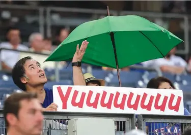  ?? Associated Press ?? A Texas Rangers fan holds up a sign for Texas Rangers pitcher Yu Darvish while checking the sky as a light rain begins to fall, delaying the start of a baseball game between the New York Yankees and the Rangers on Friday in New York.