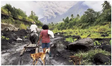  ??  ?? A rumbling Mayon Volcano spews ash as lava cascades down the slopes as seen from a village in Legazpi City, Albay yesterday. Inset shows villagers walking near the volcano despite the raised alert levels.