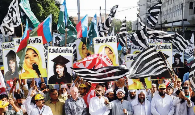  ?? Reuters ?? ↑
People carry flags and signs demanding release of Aafia Siddiqui, a Pakistani neuroscien­tist, who was sentenced to 86 years by a US judge, during a protest march in Karachi on Friday.