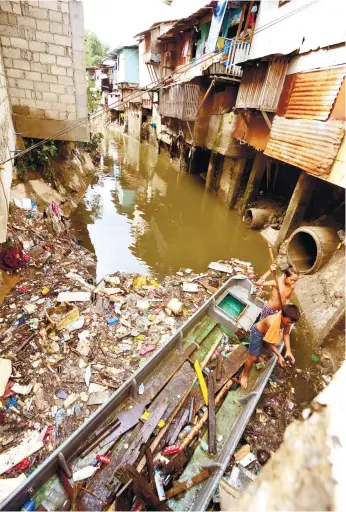  ?? (SUN.STAR FOTO/ALLAN CUIZON) ?? URBAN FISHING. Scavengers fish out items they can use or sell, from the garbage floating in Mahiga Creek, on the border between the cities of Mandaue and Cebu. The creek is so clogged that it often overflows during heavy rains. See how houses and other structures have completely taken over its banks.