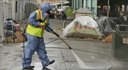  ?? Eric Risberg/Associated Press ?? A city worker uses a power washer to clean the sidewalk by a tent city along Division Street in San Francisco.