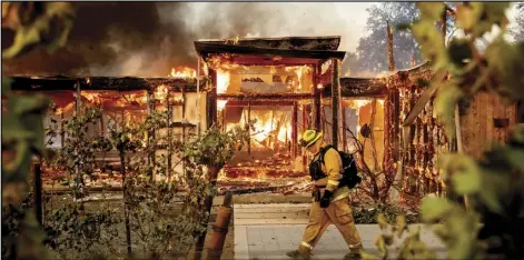  ?? AP Photo/Noah Berger, File ?? In this Oct. 27 file photo Woodbridge firefighte­r Joe Zurilgen passes a burning home as the Kincade Fire rages in Healdsburg, Calif.