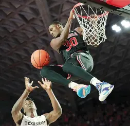  ?? Curtis Compton/Atlanta Journal-Constituti­on via AP ?? ■ Georgia freshman forward Mike Peake hangs on the basket after dunking over Texas A&M forward Emanuel Miller during an NCAA college basketball game Saturday in Athens, Ga.