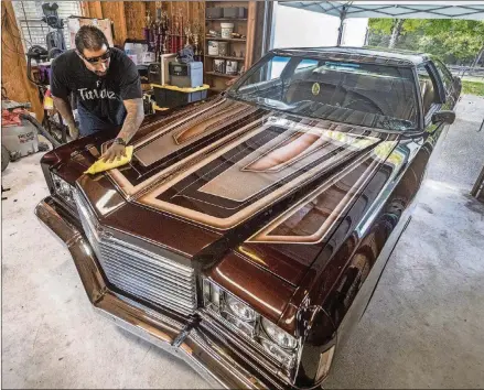  ?? BOB ANDRES/ROBERT.ANDRES@AJC.COM PHOTOS ?? Alfredo “Freddy” Quintero gives his Impala a wipe down as he waits for the Hot Wheels trailer to pick up his car for the event. Quintero and his custom 1975 Chevy Impala are to compete in the Hot Wheels Tour Grand Finale in Las Vegas today.