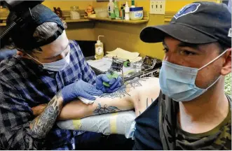  ?? MARSHALL GORBY / STAFF ?? Robert Lamb of Truth and Triumph Tattoo works on the tattoo of Tyler Milligan recently, since reopening. Companies are allowed to reopen if they follow state rules for health and safety, including requiring employees to wear face masks.