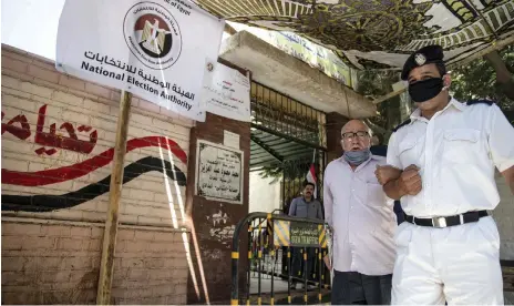  ??  ?? A police officer assists a voter at a polling station in Cairo yesterday during low turnout for the Senate election