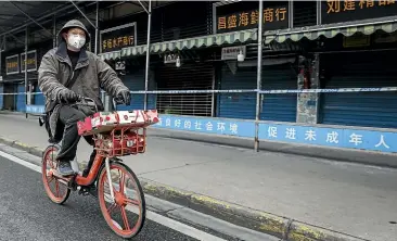 ?? GETTY IMAGES ?? A man rides past Wuhan’s closed Huanan Seafood Market on January 17.