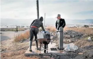  ?? ?? DURAS CONDICIONE­S
Varios inmigrante­s rellenan bidones de agua en la fuente del asentamien­to de Atochares, el más grande del municipio