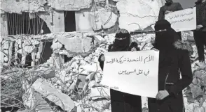  ?? HUSSEIN MALLA/AP ?? Women stand in the rubble with placards reading “United Nations are the partners of Bashar Assad and killing Syrians,” in Atareb, Syria.