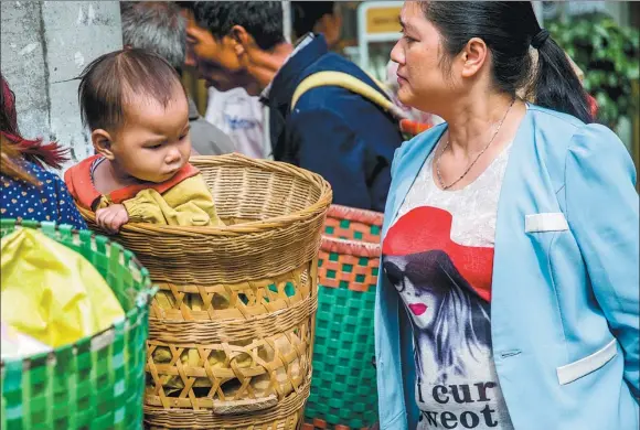  ??  ?? The pattern on the Tshirt of a rural woman catches the attention of a child next to her at a market in Yongxing town, Meitan county, Guizhou province.