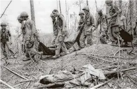  ?? Associated Press ?? American troops carry the bodies of fellow soldiers past a wounded North Vietnamese soldier on Hill 990 in South Vietnam’s central highlands on June 2, 1968. Television brought the war in Southeast Asia into living rooms across the United States.