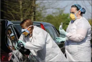  ?? The Associated Press ?? DRIVE-THRU TESTING: Nurse Mandy Stuckey reaches into a patient’s vehicle window to do a COVID-19 test as fellow nurse Tonya Green, right, looks on Wednesday at the drive-thru COVID-19 testing site at New Life Church in North Little Rock. The site, a partnershi­p between Sniffle Health and Natural State Laboratori­es will be open daily from 10 a.m.- 4p.m. through April 11.