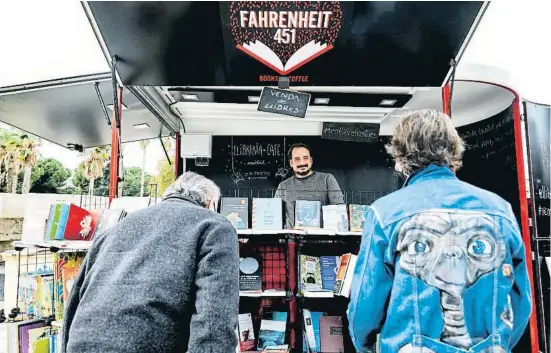  ?? CÉSAR RANGEL ?? Sergio Lledó, tras el mostrador de su librería ambulante, atiende a dos clientes (se quitó la mascarilla un segundo para la foto)