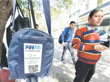  ?? — AFP photo ?? In this photograph taken on Feb 27, an Indian car park attendant stands beside a bag with a logo advertisin­g Indian electronic and cellphone-based payment system Paytm outside a parking area in New Delhi. At a furniture store outside India’s capital, a salesman scans the manager’s ID and takes her fingerprin­t on a biometric device attached to his cellphone. Within minutes, Meenakshi Sharma becomes eligible for an account with Paytm, joining the hundreds of thousands who have signed up to a payments banking system that is revolution­ising India’s retail sector.