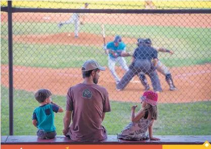  ??  ?? Daniel Kilpatric, center, from Santa Fe, along with his children Zealand, 3, right, and Zinnia, 5, watch the Santa Fe Fuego take on the White Sands Pupfish on June 9 in Santa Fe.