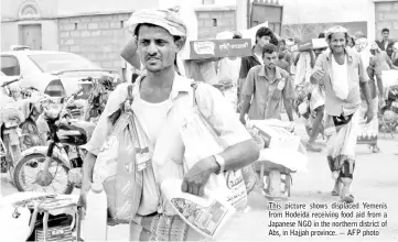  ??  ?? This picture shows displaced Yemenis from Hodeida receiving food aid from a Japanese NGO in the northern district of Abs, in Hajjah province. — AFP photo