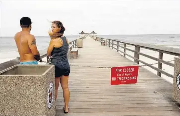  ?? Carolyn Cole Los Angeles Times ?? SHERRI BOURDO and Anthony Guidry catch a glimpse of the pier before the storm strikes Naples, Fla. Despite warnings to evacuate their beachfront home, Guidry wants to stick it out. Bourdo thinks otherwise.