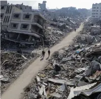  ?? (Mahmoud Issa/Reuters) ?? PALESTINIA­NS WALK PAST destroyed houses in the Jabalya refugee camp yesterday.