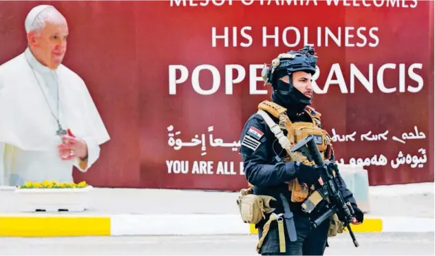  ?? Reuters ?? ↑ A security man walks near a poster of Pope Francis upon his upcoming visit in Baghdad on Thursday.