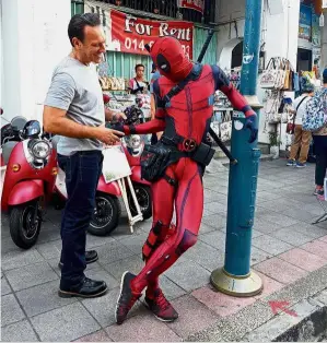  ??  ?? Nice to meet you: Mohamad Syukur dressed as ‘Deadpool’ greeting a tourist near Armenian Street in Penang.