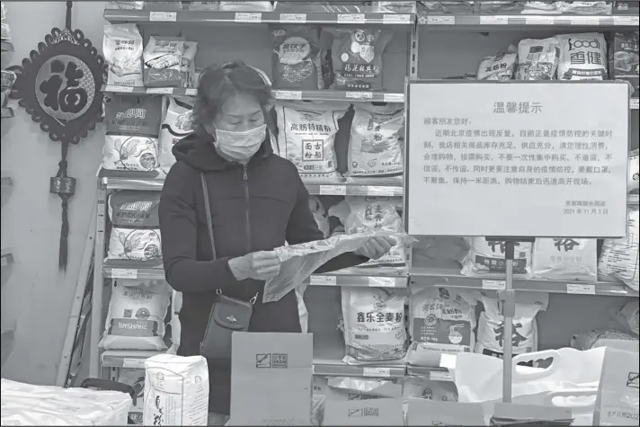  ?? NG HAN GUAN/AP ?? A woman wearing a mask shops near a sign which calls for shoppers to be vigilant against the coronaviru­s rebounding and not to listen to rumors and to avoid stockpilin­g at a supermarke­t in Beijing, China, Wednesday. A recent seemingly innocuous government recommenda­tion for Chinese people to store necessitie­s for an emergency quickly sparked scattered instances of panic-buying and online speculatio­n of imminent war with Taiwan.