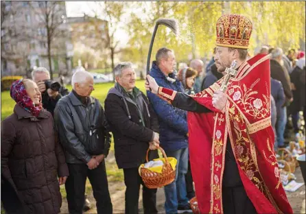  ?? ?? An orthodox Ukrainian priest blesses believers as they collect traditiona­l cakes and painted eggs prepared for an Easter celebratio­n during a religious service at a church in Bucha, on the outskirts of Kyiv, on April 24, 2022. (AP)