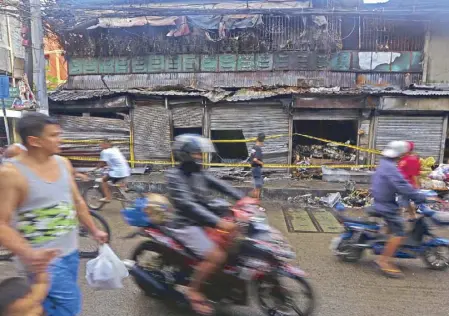  ?? ERNIE PENAREDOND­O ?? People pass by a commercial building at the corner of Taniman Avenue and Bayabas street in Pasig City that was destroyed by a fire before dawn yesterday.