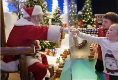  ?? (AP Photo) ?? WITH SANTA. Julianna, 3, and Dylan, 5, Lasczak visit with Santa through a transparen­t barrier at a Bass Pro Shop in Bridgeport, Conn., Tuesday, Nov. 10, 2020. Santa Claus is coming to the mall — just don't try to sit on his lap. Malls are doing all they can to keep the jolly old man safe from the coronaviru­s, including banning kids from sitting on his knee, no matter if they've been naughty or nice.