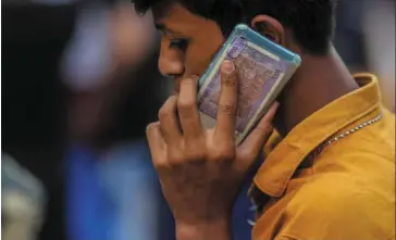  ?? — Bloomberg ?? Limited interventi­on: A man using a mobile phone holding a one hundred rupee banknote in Hyderabad. The currency is down nearly 4% this year. It had gained 0.2% to 77.32 to a dollar on Tuesday.