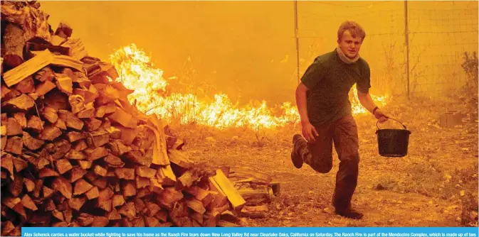  ?? — AFP ?? Alex Schenck carries a water bucket while fighting to save his home as the Ranch Fire tears down New Long Valley Rd near Clearlake Oaks, California on Saturday. The Ranch Fire is part of the Mendocino Complex, which is made up of two blazes, the River Fire and the Ranch Fire.