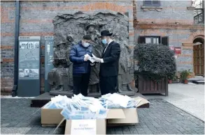  ?? (Chabad of Shanghai) ?? CHABAD EMISSARIES distribute masks in front of the monument rememberin­g Jewish refugees who found shelter in Shanghai, in the area known as the Hongkou ghetto.