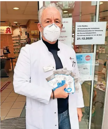  ?? FOTO: KURT LEHMKUHL ?? Roland Kiel steht vor seiner Apotheke, an deren Eingangstü­re ein Schild auf die bevorstehe­nde Verteilung hinweist. Er hat zwar FFP2-Masken bestellt, will aber erst am 21. Dezember mit der Abgabe beginnen.